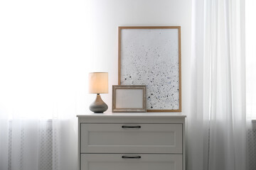 Modern chest of drawers with lamp near window indoors