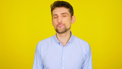 Handsome bearded man flirts licking lips with teeth on yellow background with copy space. Sexy guy in light blue shirt with closed eyes. Place for text or product - obrazy, fototapety, plakaty