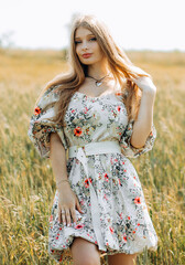 Busty sweet blonde in a beige dress with a print poses in a wheat field.