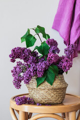Purple lilacs in a basket on a stool and purple towel hanging on a wall