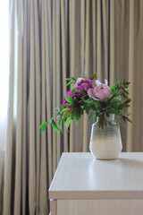 Pink peonies in a vase and grey curtains in the background