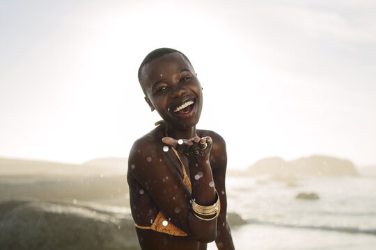 African woman blowing confetti from her hand on the beach