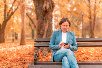 Woman typing text message on mobile phone on park bench