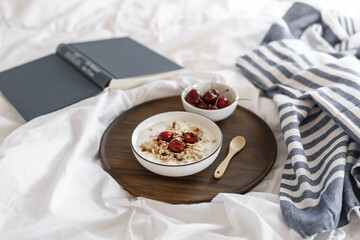 Müsli mit frischen Kirschen und Joghurt auf einem Holzserviertablett auf einer weißen Bettdecke....