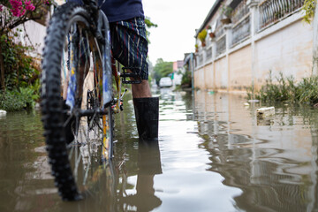 Legs with rubber boots in flooding,Asian man wear waterproof boots with his old bicycle in flooding,after heavy rainfall on the street,person riding a bicycle on a flood,storm during the rainy season