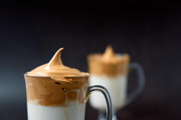Close up of glasses of trendy fluffy creamy dalgona or whipped instant coffee with milk on the dark background. New popular food and drink trend concept. Copy space.
