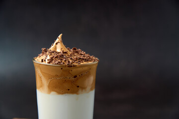 Close up of glass of trendy fluffy creamy dalgona or whipped instant coffee with milk and chocolate on the dark background. New popular food and drink trend concept. Copy space.