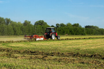 Fototapeta premium Tractor working at field Haymaking in the countryside Beautiful scenery and blue sky.