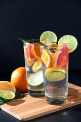 Health care, fitness, healthy nutrition diet concept. Fresh cool homemade citrus infused detox water with grapefruit, orange, lemon and lime and ice in glasses on dark background.