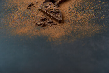 Dark chocolate stack, chips and cocoa powder on a dark background. Confectionery and food concept. Top view, copy space, selective focus..