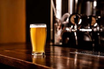 Light beer in glass. Ale with foam on brown wooden counter, metal taps near
