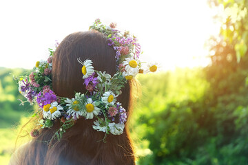 girl in summer solstice wreath outdoor. rear view of woman with brown hair and flowers wreath....