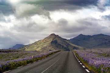 A road with colorful mountains and impressive clouds in the background
