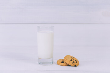 Oatmeal cookies with chocolate on a light background with a glass of milk.