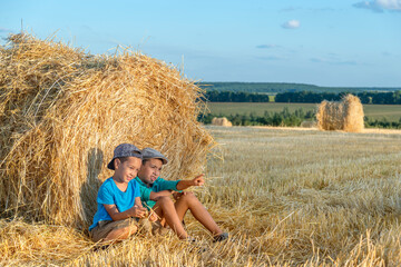  Children  sit at a haystack in a field with hay bales after harvest on a sunny day and have fun talking