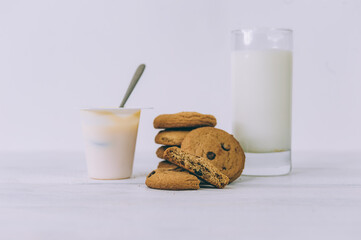 Oatmeal cookies with chocolate on a light background with a glass of milk and yogurt.