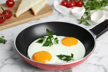 Tasty cooked chicken eggs with parsley in frying pan on white marble table, closeup