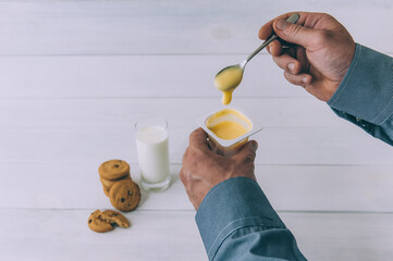 A man holds yogurt in his hand on a background of oatmeal cookies and a glass of milk.