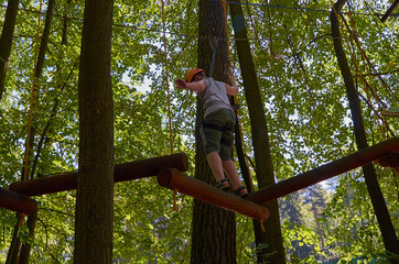 Naklejka na ściany i meble A boy with a helmet and insurance passes a high-altitude obstacle course.