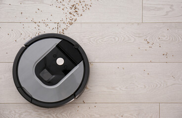 Modern robotic vacuum cleaner removing scattered buckwheat from wooden floor, top view. Space for...