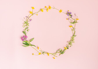 Fresh rustic wildflowers lined with a round frame on delicate pastel pink background. Template greeting card copy space