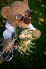 Soft toy bear in sunglasses at sunset, a wedding bouquet, grass, wedding.