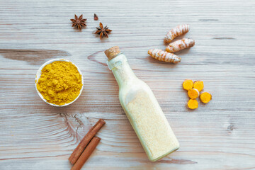 Goldene Milch mit Kurkuma in einer Glasflasche, Zimtrinde, Sternanis und einem Schüssel mit Pulver auf einem Holz Hintergrund. Draufsicht, Aryuveda, Indien, Zutaten. © Sonja Rachbauer
