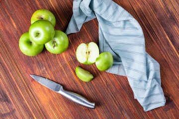 High angle shot of some green apples and a knife and a tablecloth on a wooden surface