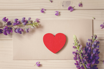 flat lay red vintage wood heart lies on craft envelope on rustic table with bouquet of flowers lupine, concept love, message