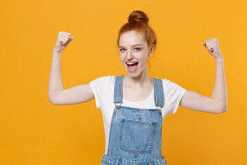 Strong young readhead girl in casual denim clothes white t-shirt isolated on yellow background studio portrait. People sincere emotions lifestyle concept. Mock up copy space. Showing biceps, muscles.