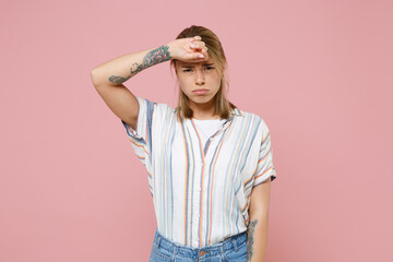 Exhausted tired young blonde woman girl in casual striped shirt posing isolated on pastel pink wall background studio portrait. People emotions lifestyle concept. Mock up copy space. Put hand on head.