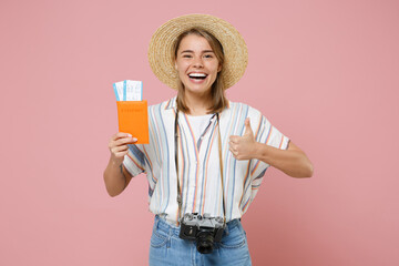 Funny young girl in striped shirt hat with photo camera isolated on pink background. Passenger traveling abroad on weekends getaway. Air flight journey concept. Hold passport tickets showing thumb up.