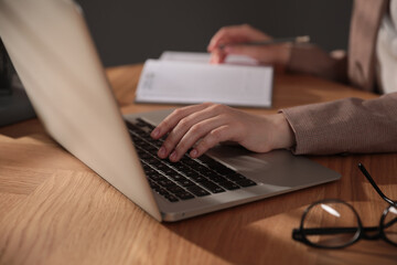 Woman working with laptop at wooden desk indoors, closeup