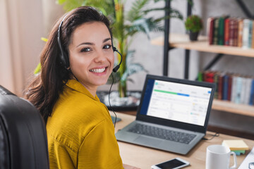 Portrait of beautiful freelancer female posing and working online with headset and looking at camera