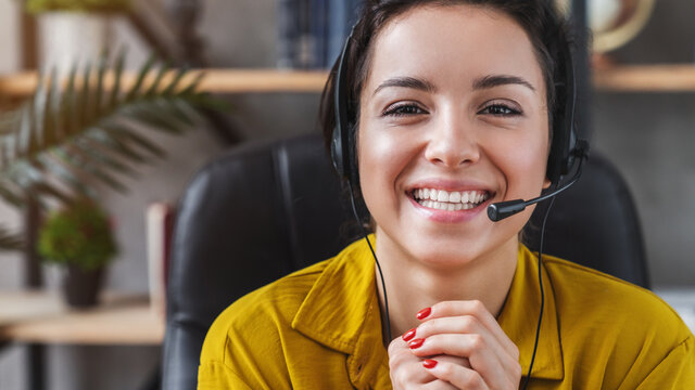 Happy young woman wear headset communicating by conference call speak looking at computer at home office