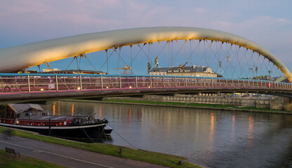 Fototapeta na wymiar Father Bernatek Footbridge lit up at sunset with the Vistula River in Krakow, Poland