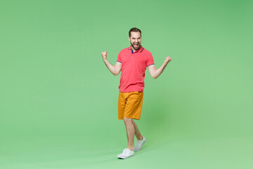 Fototapeta na wymiar Joyful young bearded man guy in casual red pink t-shirt posing isolated on green background studio portrait. People sincere emotions lifestyle concept. Mock up copy space. Clenching fists like winner.