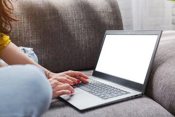 Close up of female sit on sofa and typing on laptop with mockup screen