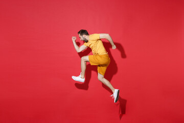 Fototapeta na wymiar Side view of screaming young bearded man guy in casual yellow t-shirt posing isolated on red background studio portrait. People emotions lifestyle concept. Mock up copy space. Jumping like running.