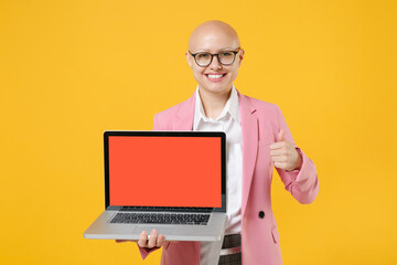 Smiling bald business woman in white shirt pink jacket glasses isolated on yellow wall background. Achievement career wealth concept. Hold laptop pc computer with blank empty screen, showing thumb up.
