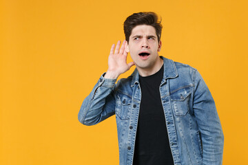 Curious young man guy in casual denim jacket posing isolated on yellow background studio portrait....