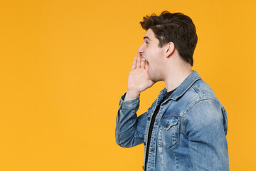 Side view of crazy young man guy in casual denim jacket posing isolated on yellow wall background studio portrait. People lifestyle concept. Mock up copy space. Screaming with hand gesture near mouth.