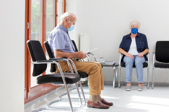 Senior woman and man sitting with face masks in a bright waiting room of  a hospital or an office