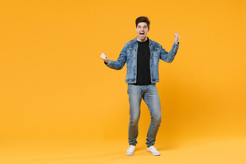 Fototapeta na wymiar Screaming young man guy wearing casual denim clothes posing isolated on yellow background studio portrait. People sincere emotions lifestyle concept. Mock up copy space. Clenching fists like winner.