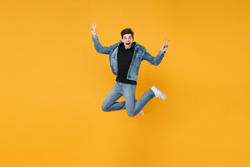 Fototapeta na wymiar Screaming young man guy wearing casual denim clothes posing isolated on yellow background studio portrait. People sincere emotions lifestyle concept. Mock up copy space. Jumping, showing victory sign.