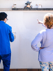 Man and woman painting the wall of the house terrace. Back view of mature couple reforming the home.