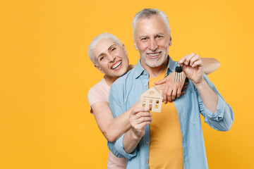 Cheerful elderly gray-haired couple woman man in casual clothes isolated on yellow background studio portrait. People emotions lifestyle concept. Mock up copy space. Hold house bunch of keys, hugging.