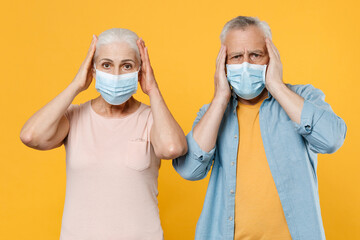 Elderly gray-haired couple woman man in casual clothes sterile face mask isolated on yellow wall background. Epidemic pandemic coronavirus 2019-ncov sars covid-19 flu virus concept. Put hands on head.