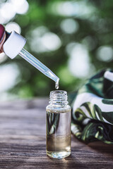 Essential oil falling from glass dropper. Dropper with aroma oil. Glass bottle of aroma oil isolated on wooden table. Spa Treatment.