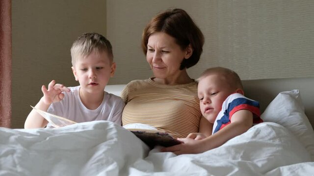 Mother and her children reading a book. toddler boys in bed, caring a child